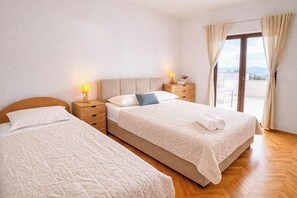 Habitació d'hotel amb dos llits, terra de fusta, balcó i vista, i una tauleta de nit amb una làmpada.