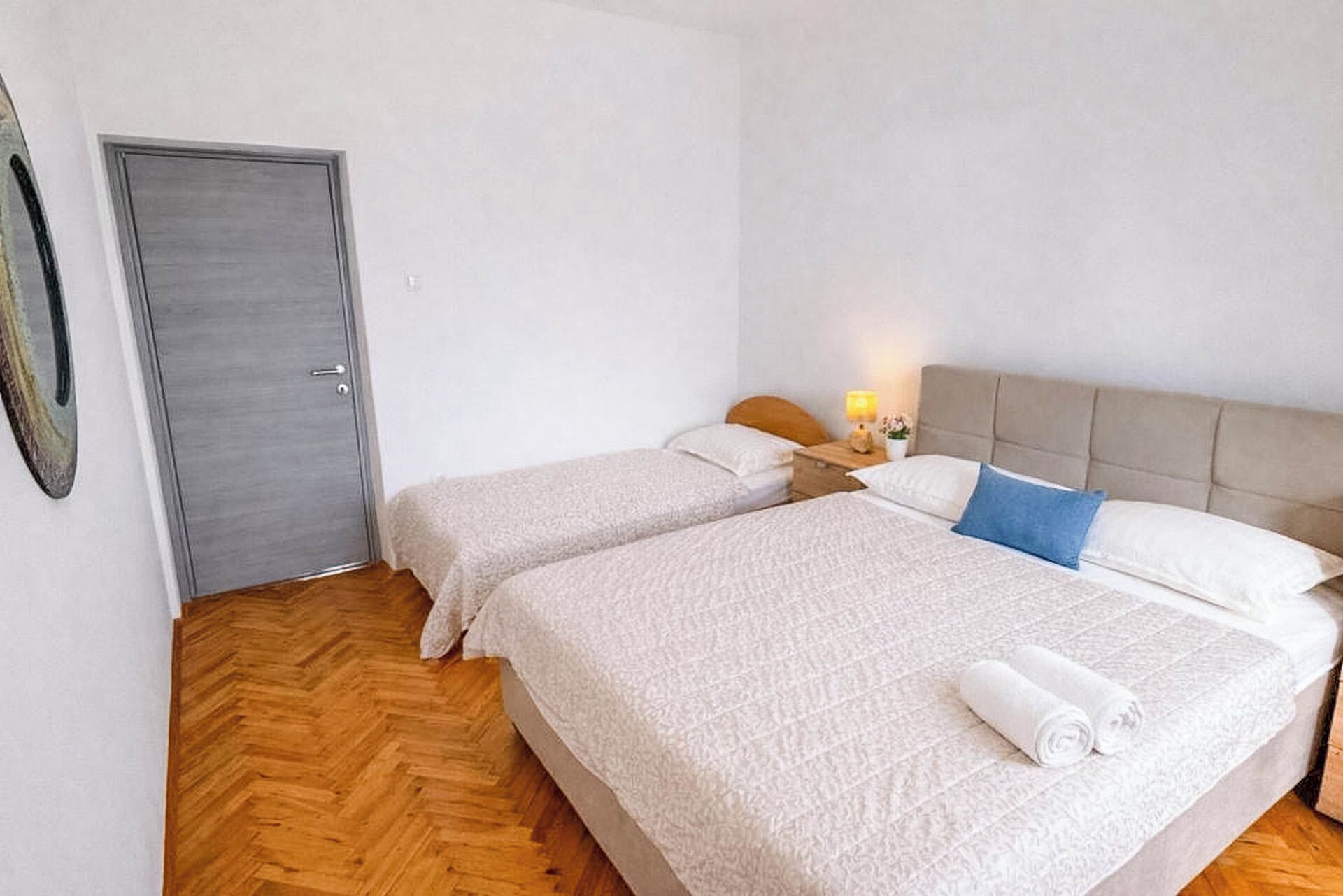 Une chambre avec deux lits, un plancher en bois, une porte et une table de chevet avec une lampe.