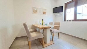 Ein Essbereich mit Tisch und Stühlen, einer Weinflasche und einem an der Wand befestigten Fernseher.