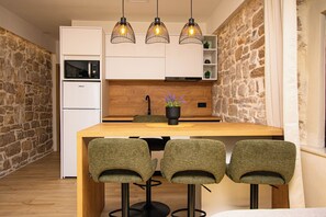 Eine moderne Küche mit einem Holztisch, drei Barhocker, einem Einbauofen und Pendelleuchten.