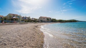 A pebbled beach with clear water, houses with red roofs, and a clear sky. - Apartment Blue Wind (Tkon)