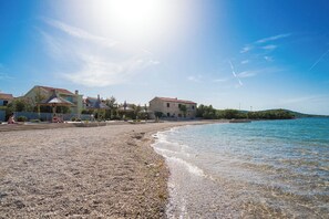 A pebbled beach with clear water, houses with red roofs, and a clear sky. - Apartment Blue Wind (Tkon)
