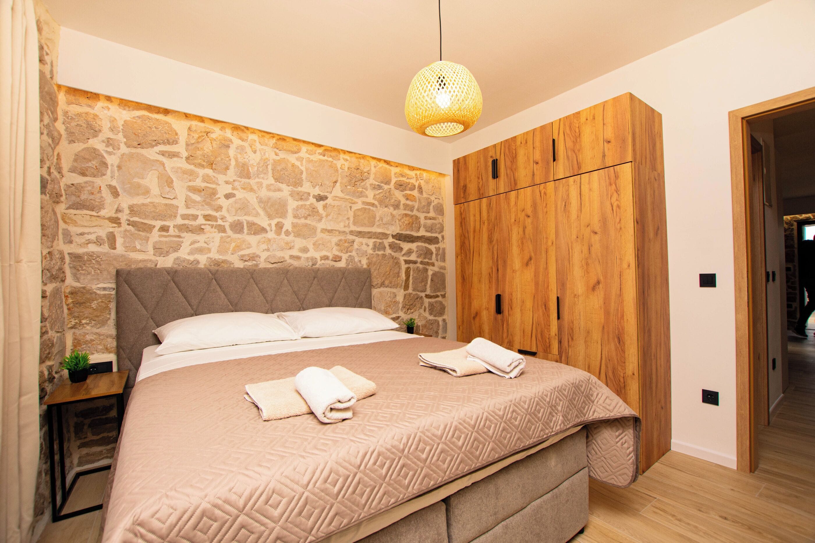 Een slaapkamer met een stenen muur, een houten garderobe, een bed met hoofdeinde en een hanglamp.