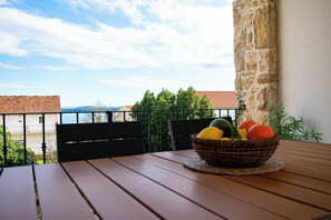 Ein Balkon mit einem Korbwäscher voller Früchte auf einem Holztisch, mit Blick auf eine Wohngegend mit roten Ziegeldächern und viel Grün.