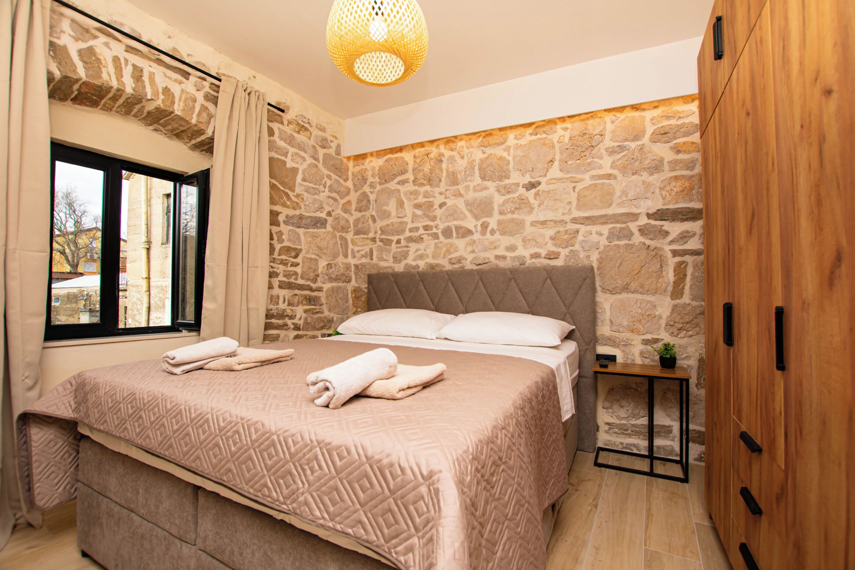 Un dormitorio con pared de piedra, una cama con colcha estampada, una mesita de noche con una planta y un armario.