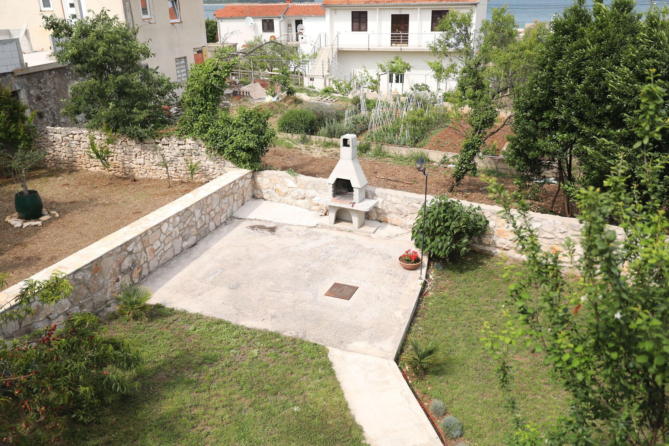 Zona patio con muro in pietra, barbecue e vegetazione circostante.