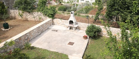 A patio area with a stone wall, a grill, and surrounding greenery.