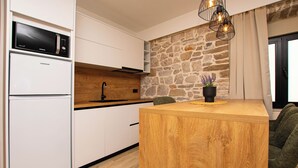 A modern kitchen with white cabinetry, a stone accent wall, a wooden island, and a built-in microwave. - Apartment Blue Wind (Tkon)