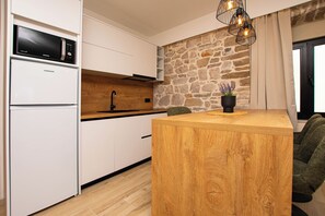 A modern kitchen with white cabinetry, a stone accent wall, a wooden island, and a built-in microwave. - Apartment Blue Wind (Tkon)