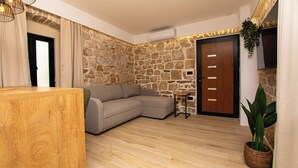 A room with a wooden reception desk, a beige sofa, a stone wall, a wooden door, and a potted plant. - Apartment Blue Wind (Tkon)