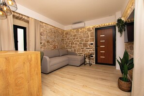 A room with a wooden reception desk, a beige sofa, a stone wall, a wooden door, and a potted plant. - Apartment Blue Wind (Tkon)
