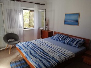 Ein Schlafzimmer mit einem Bett, einem Sessel, einem Fenster und einem Bild an der Wand.