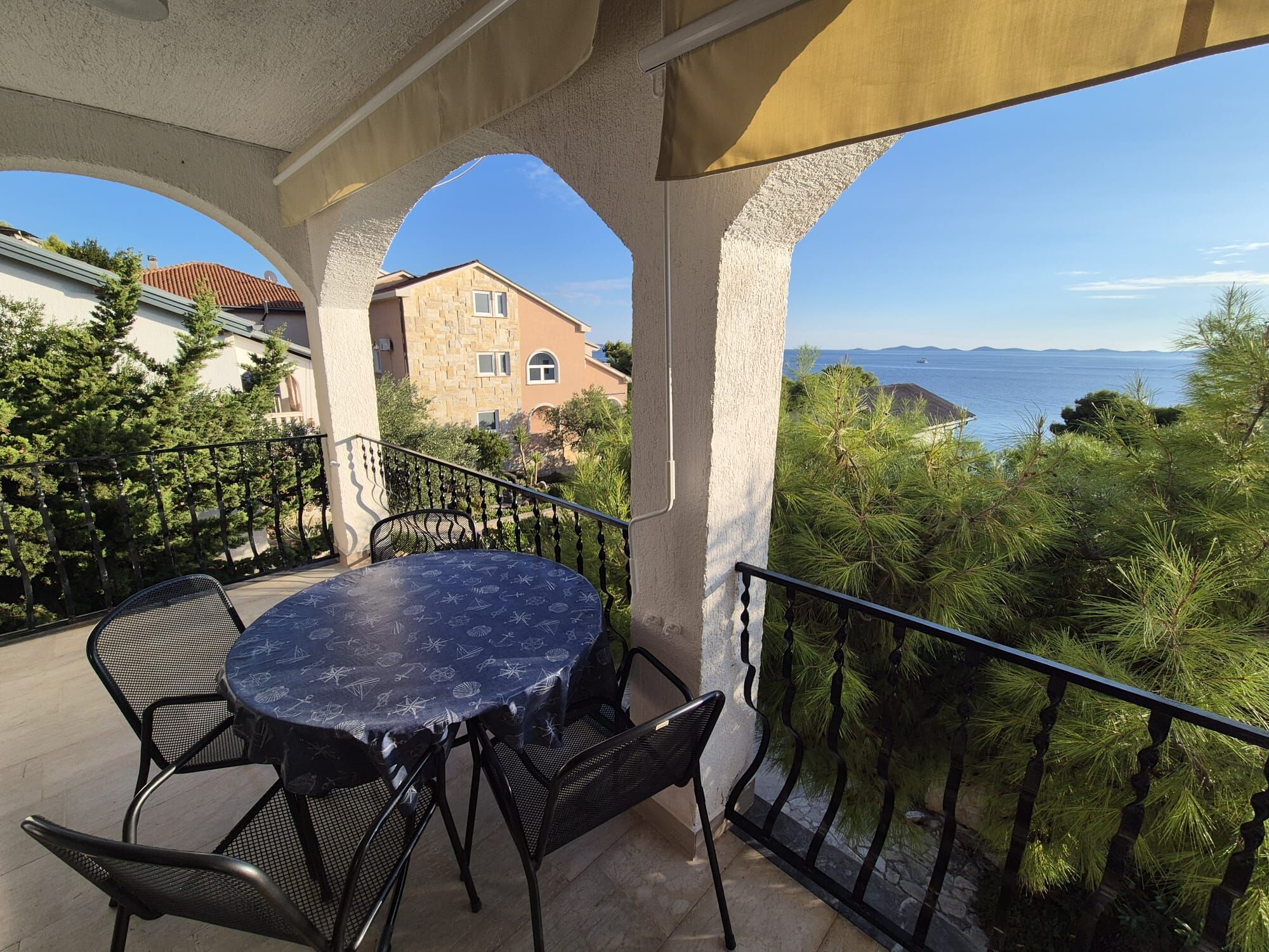 Un balcon avec une table ronde et des chaises, offrant une vue sur la côte, avec des maisons et des arbres.