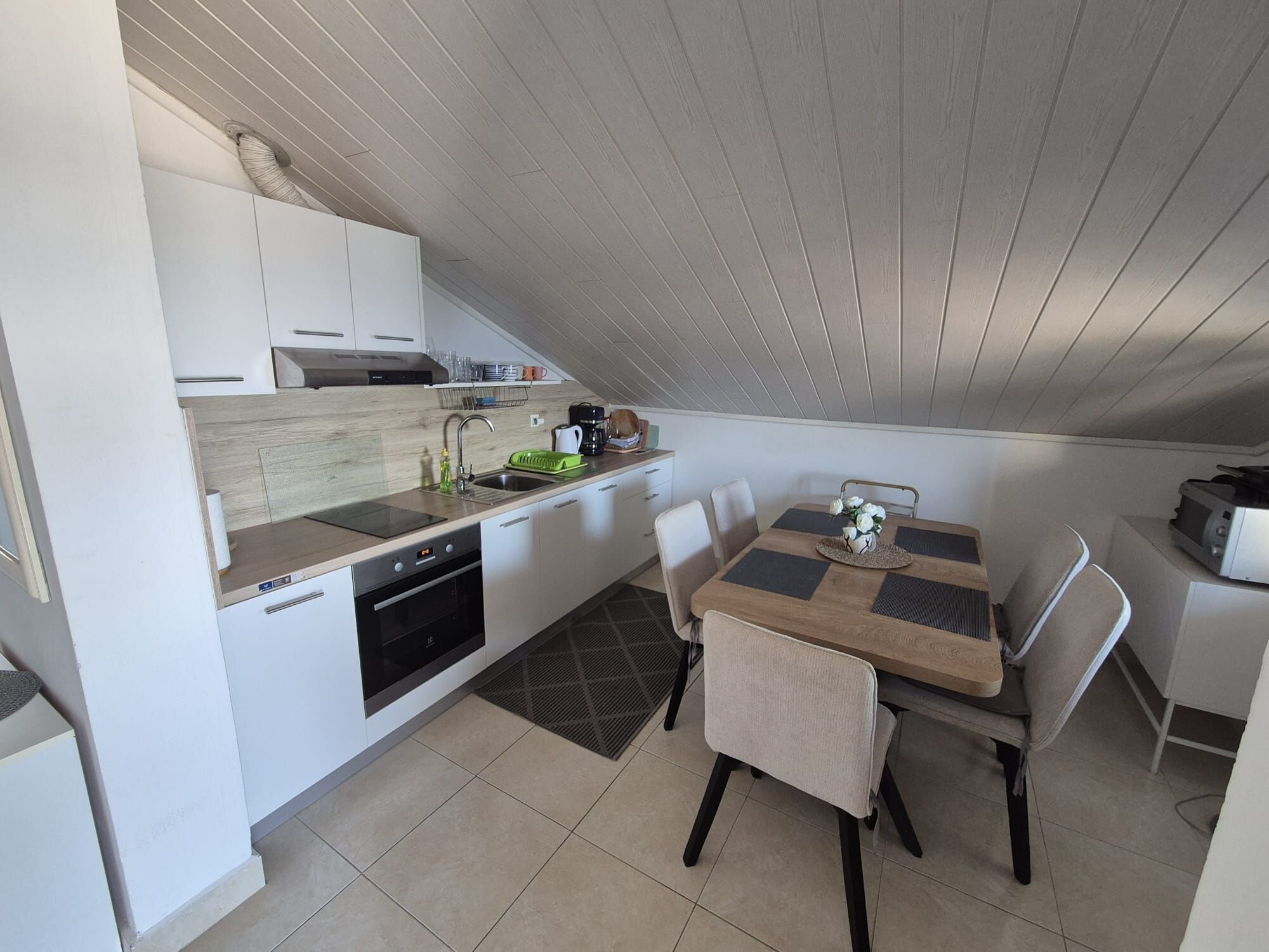 Cocina compacta con lavavajillas, horno y comedor con mesa y sillas.