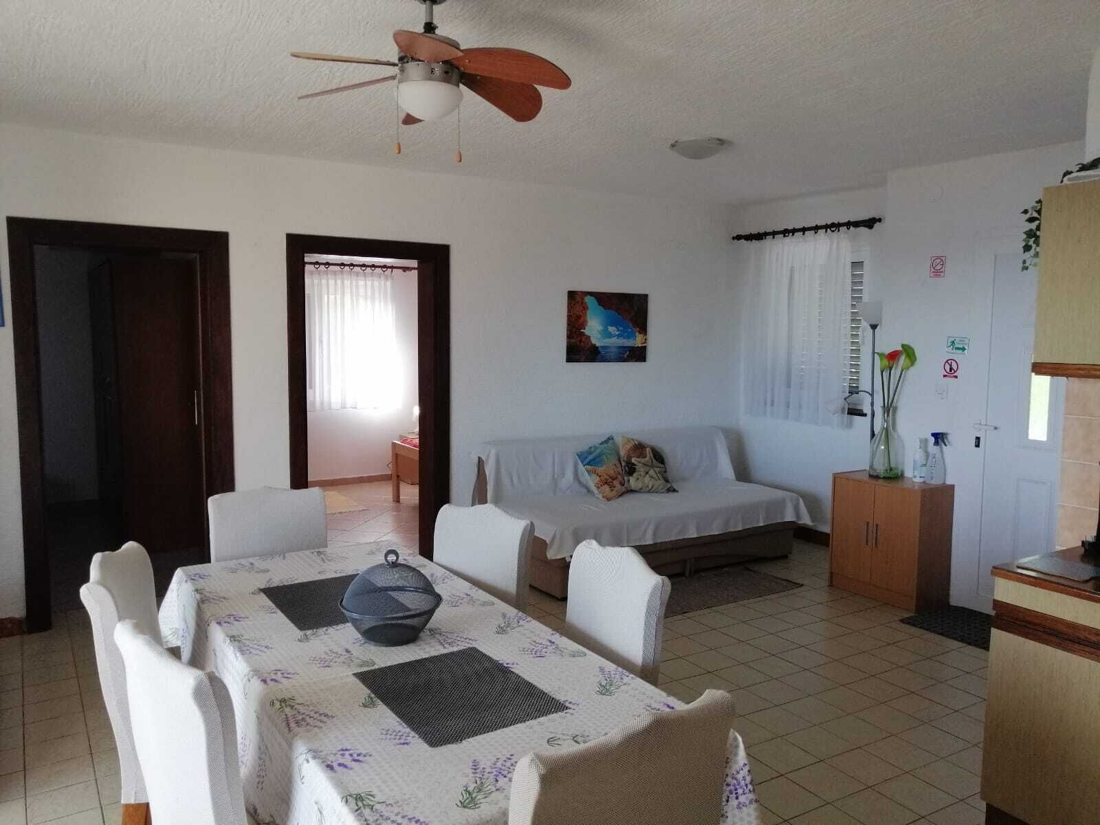 A dining area with a table set for four, a ceiling fan, a sofa, and a cabinet with decorative items.
