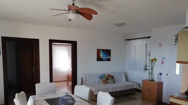 Ein Essbereich mit einem Tisch für vier Personen, einem Deckenventilator, einer Couch und einem Schrank mit Dekoration.