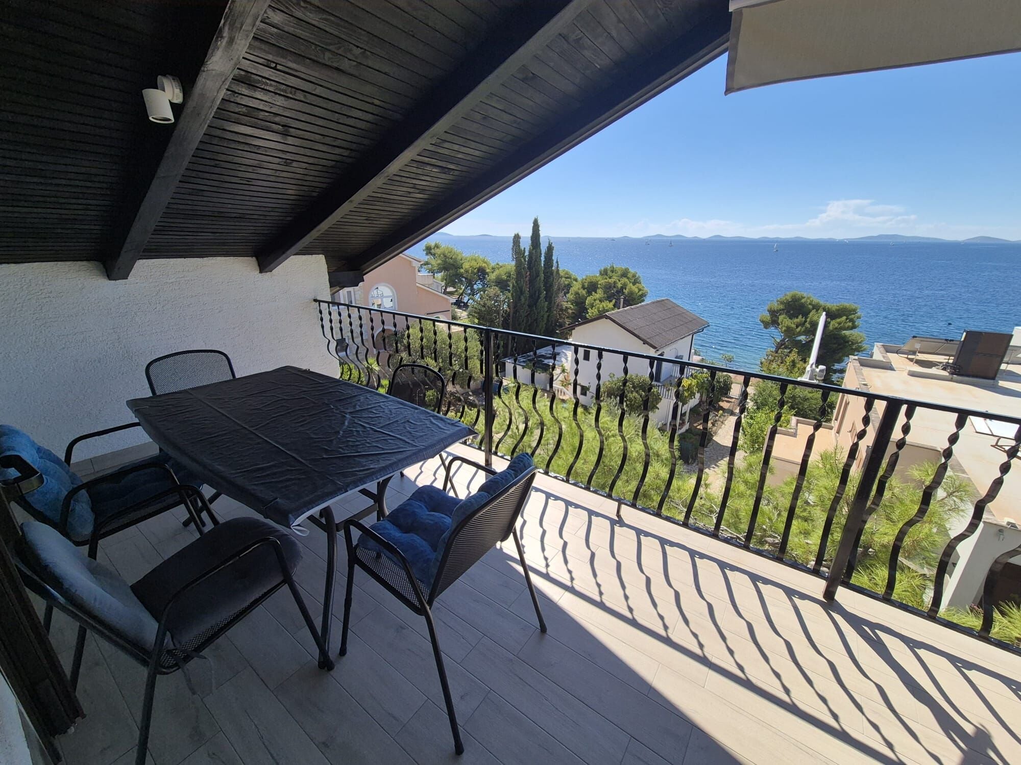 A balcony with a table and chairs, overlooking a body of water and a distant coastline.