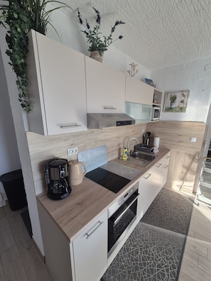 A modern kitchen with white cabinets, a black countertop, and a built-in oven. - Apartments Sepcevic (Murter-Kornati)