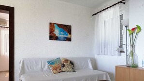 Ein Zimmer mit einem weißen Sofa, einem Gemälde einer Küstenszene, einer Vase mit Blumen und einem Schrank.