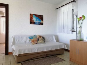 Ein Zimmer mit einem weißen Sofa, einem Gemälde einer Küstenszene, einer Vase mit Blumen und einem Schrank.