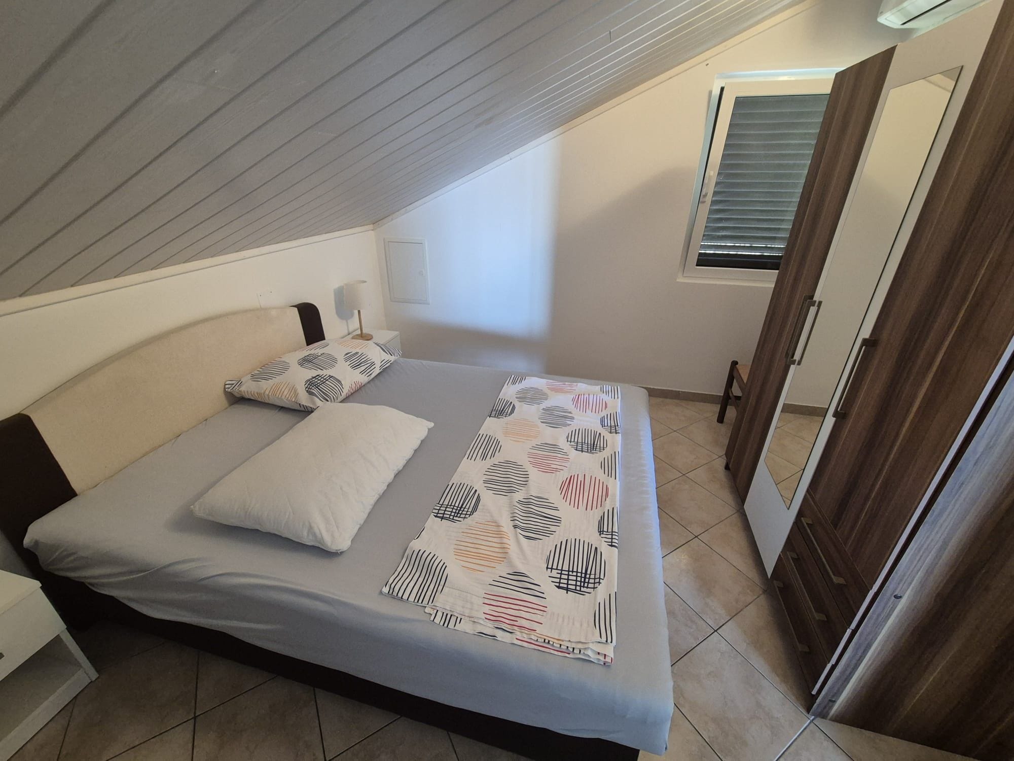 Quarto com cama, almofadas, mesa de cabeceira, janela e porta.