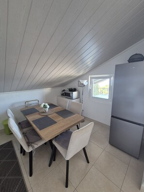 A compact kitchen with a dining table, chairs, a refrigerator, and a window. - Apartments Sepcevic (Murter-Kornati)