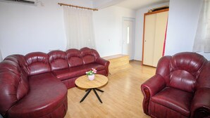 A living room with a sectional sofa, a single armchair, a small round table, and a wooden floor. - Apartment Nikol (Crikvenica)