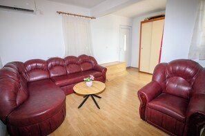 A living room with a sectional sofa, a single armchair, a small round table, and a wooden floor. - Apartment Nikol (Crikvenica)