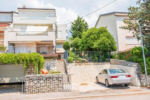 A residential street with a parked car, stone walls, and a tree. - Apartment Nikol (Crikvenica)
