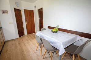A dining area with a table set for four, a wooden floor, and two wooden doors. - Apartment Nikol (Crikvenica)