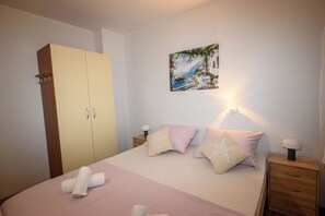 A bedroom with a bed, a wardrobe, a nightstand, and a wall-mounted picture. - Apartment Nikol (Crikvenica)