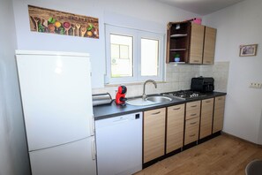 A kitchen with a white refrigerator, a toaster, a sink, wooden cabinets, and a window. - Apartment Nikol (Crikvenica)