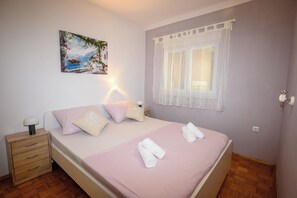 A bedroom with a bed, bedside table, lamp, and a painting on the wall. - Apartment Nikol (Crikvenica)