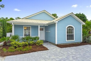 Ein zweigeschossiges Haus mit blauer Fassade, einer Veranda und einem kleinen Garten.
