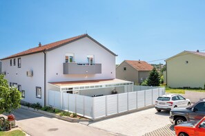 Une maison à deux étages avec un balcon, un jardin clôturé et des voitures garées.
