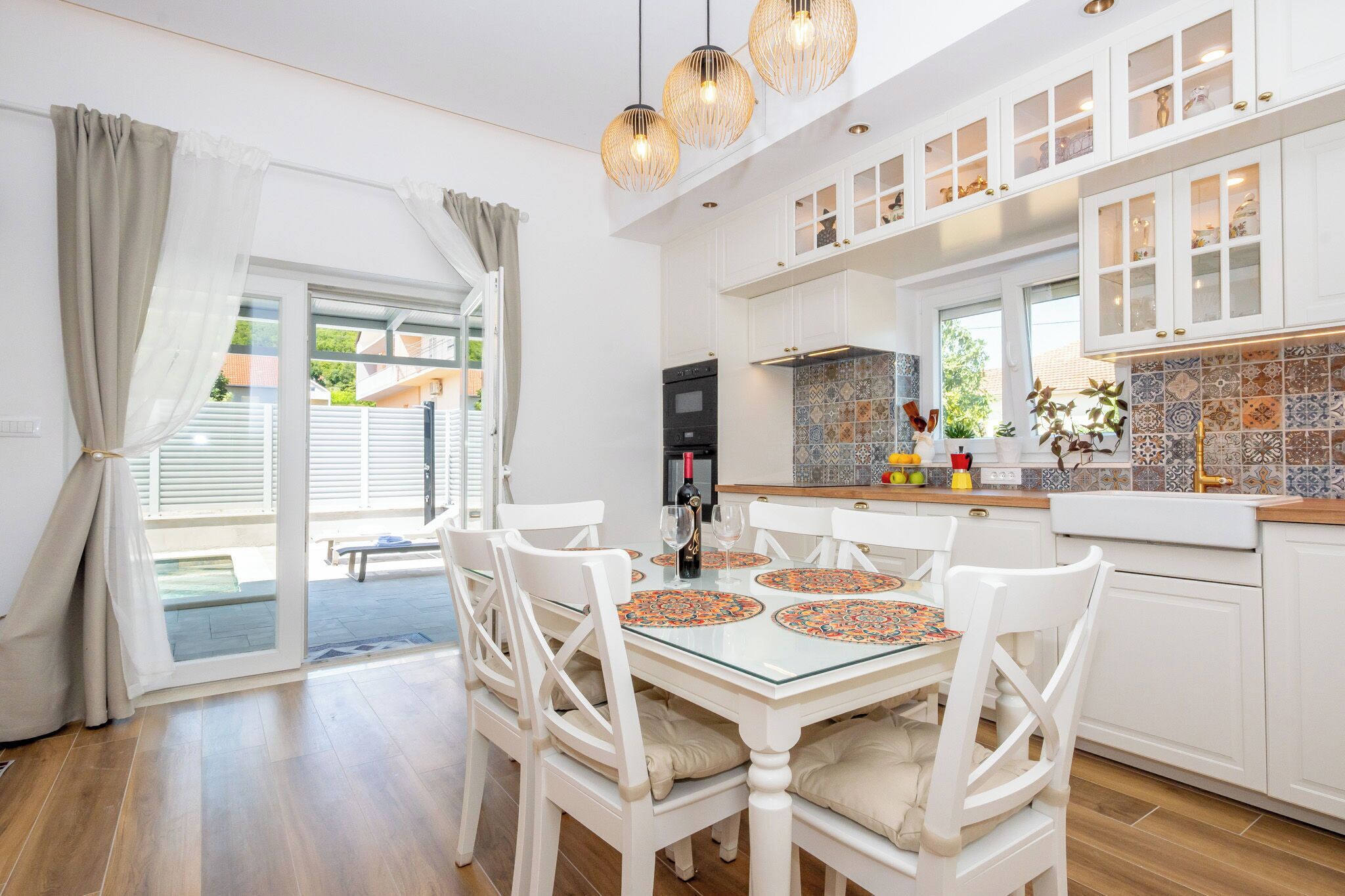 A modern kitchen with white cabinetry, a dining area with a glass table, and a view to the outside.