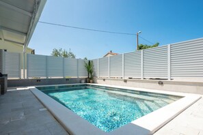 Ein rechteckiger Pool mit klarem, blauem Wasser, umgeben von einer gefliesten Terrasse und einem weißen Zaun.