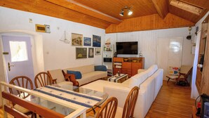 A cozy living room with a wooden ceiling, a dining area with a glass table, and a TV in the background. - House Arija (Novi Vinodolski)
