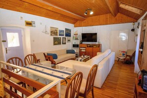 A cozy living room with a wooden ceiling, a dining area with a glass table, and a TV in the background. - House Arija (Novi Vinodolski)