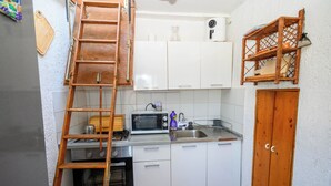 A compact kitchen with white cabinets, a microwave, a stove, and a wooden ladder. - House Arija (Novi Vinodolski)