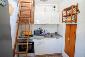 A compact kitchen with white cabinets, a microwave, a stove, and a wooden ladder. - House Arija (Novi Vinodolski)