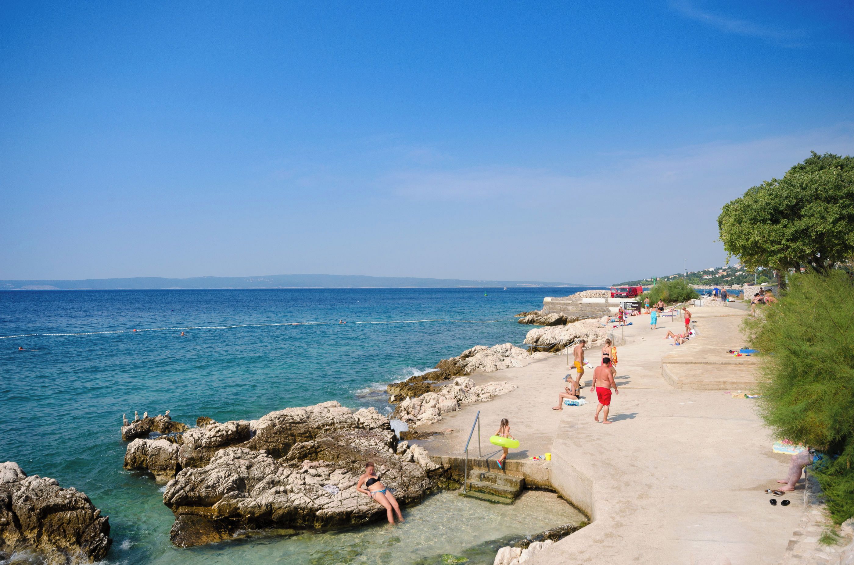Une promenade en bord de mer, avec une eau cristalline, des formations rocheuses et des gens qui profitent de la plage.