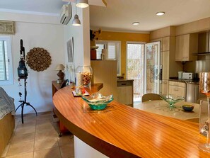 A modern kitchen with a wooden countertop, a dining area with a glass table, and a kitchen island. - Holiday Home 'Playa Y Relax' with Private Terrace, Wi-Fi and Air Conditioning (Can Picafort)
