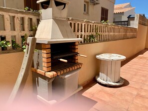 A brick-built outdoor oven with a chimney, a small round table, and a tiled patio. - Holiday Home 'Playa Y Relax' with Private Terrace, Wi-Fi and Air Conditioning (Can Picafort)
