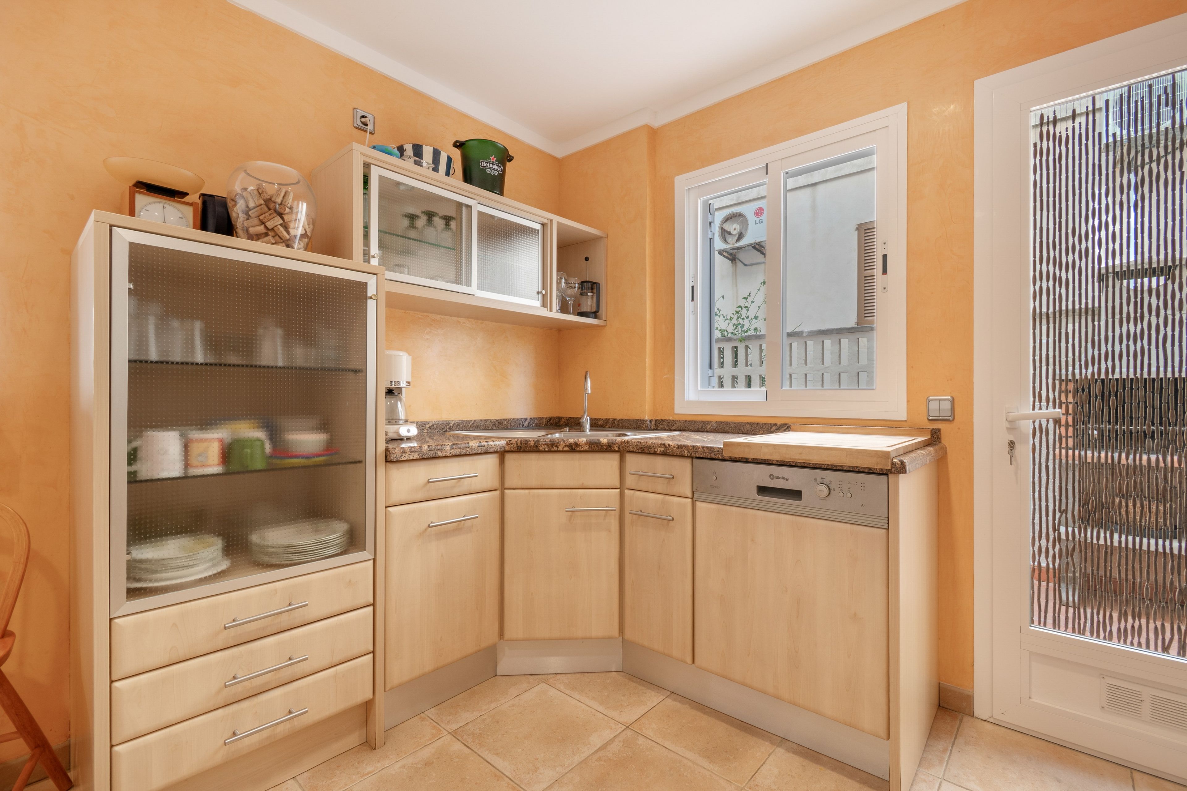 A compact kitchen with wooden cabinets, a built-in dishwasher, and a window with a view of the outside.