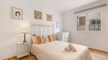 A bedroom with a bed, a nightstand, a lamp, a dresser, and a window with shutters.