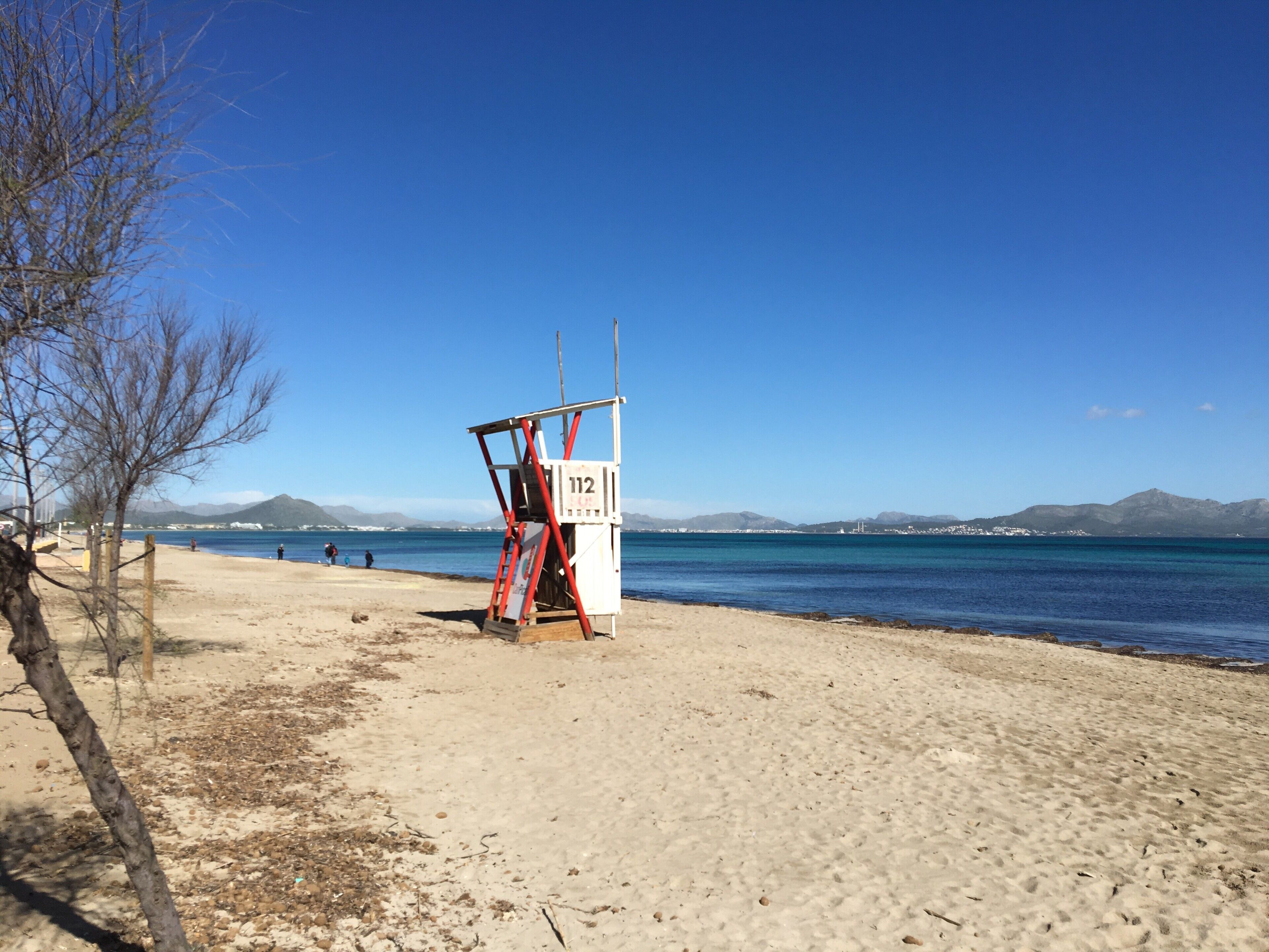Ein Rettungsturm am Strand, mit blauem Himmel und Bergen im Hintergrund.
