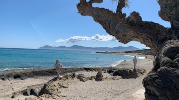 A beach with a rocky foreground and a clear view of the sea and distant mountains.