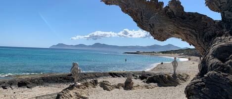 A beach with a rocky foreground and a clear view of the sea and distant mountains.