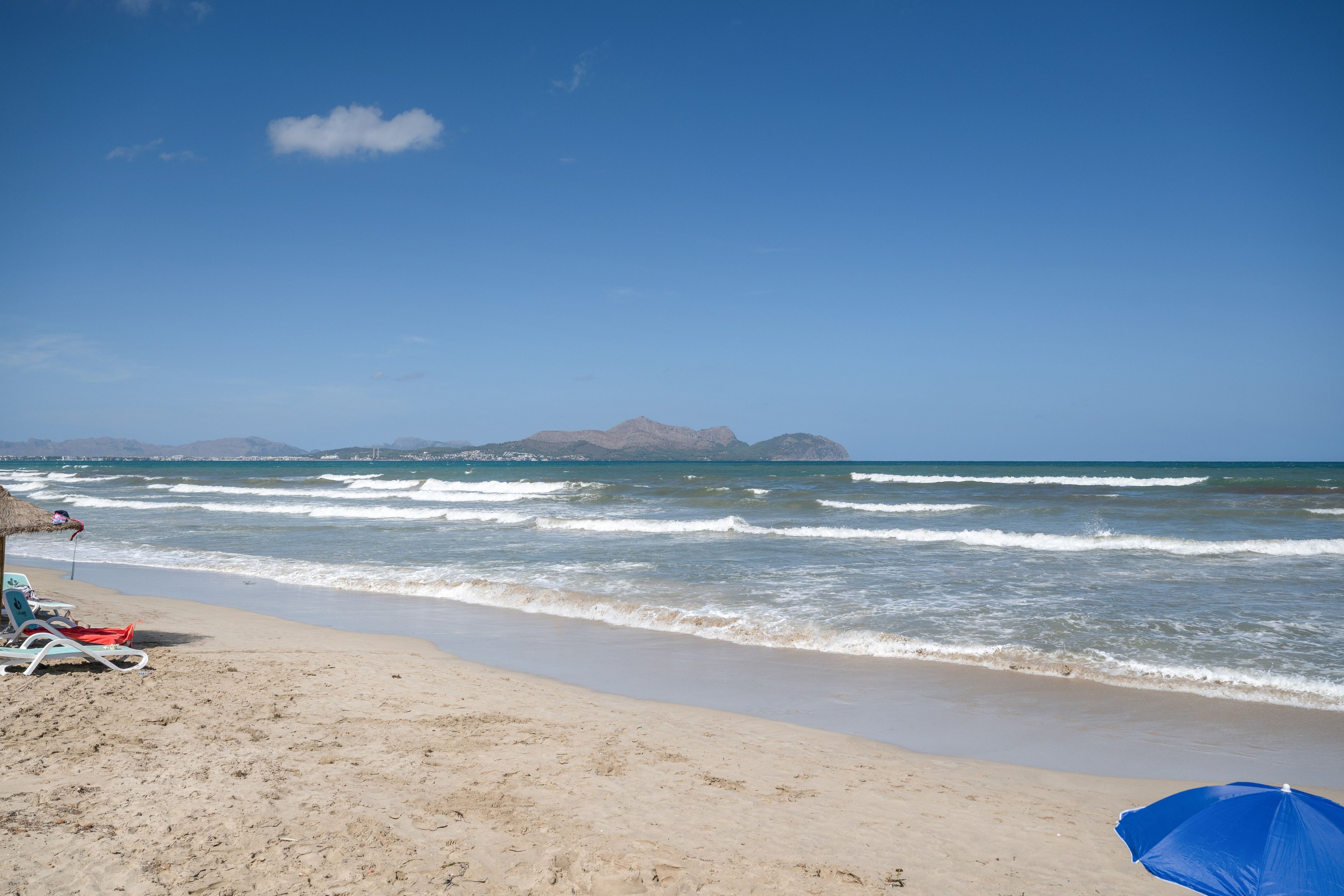 A beach with clear skies, waves, and distant mountains.